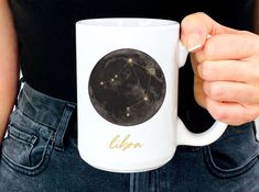 a woman holding a coffee mug with the zodiac sign libra on it's side