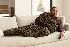 a man is sitting on a couch wrapped in a blanket and smiling at the camera