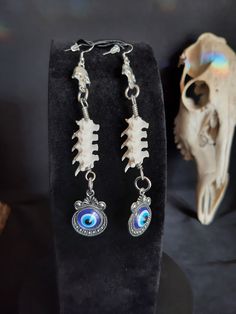 These are Gorgeous Evil Eye Earrings! They are Said to Keep Foul Energies and Intents Away From You. These Were Made with Real Rattlesnake Vertebrae. The Hooks Are Stainless Steel. These Earrings are 5 Inches Long. All Items Ship Within 1-3 Days via USPS First Class Service. Shipping on These Earrings Will be 5.00 Additional Items are Free! International Shipping Will Be 20.00, And All Additional Items Are FREE! International Shipping May Take 2 - 6 Weeks To Deliver. I Always Love to Accommodate Custom Orders! If you Have Something in Mind , Please Message me. Have a Drawing or a Photo of Your Inspiration and Send it to Me! And Also Please Send Me Your Preferred Budget For Your Piece, To Make Sure You are Not Overcharged. I DO NOT Carry Human Bones or Any Sort Of Illegal Items. And As Etsy Unique Bone-colored Nickel-free Earrings, Bone Color Dangle Earrings With Ear Wire, Nickel-free Bone Dangle Earrings, Nickel-free Bone-colored Dangle Earrings, Nickel Free Bone Color Dangle Earrings, Bone Colored Metal Earrings For Pierced Ears, Gothic White Dangle Jewelry, White Gothic Dangle Jewelry, Bohemian Bone-colored Pierced Earrings