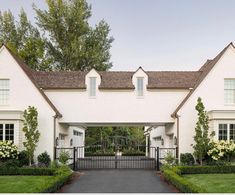 a white house with an iron gate in front of it and flowers on the driveway