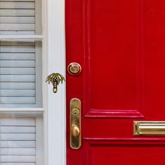 a red door with two white shutters and a gold handle on the front door