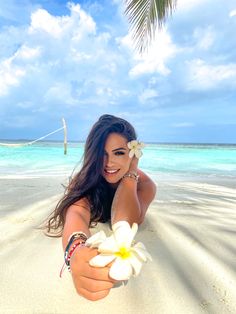 a woman laying on top of a sandy beach next to the ocean holding a flower