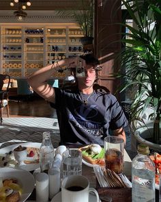 a man sitting at a table with food and drinks in front of him on his cell phone