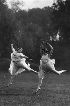 two women in white dresses are dancing on the grass