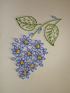 some blue flowers and green leaves on a white surface with stitched thread in the middle