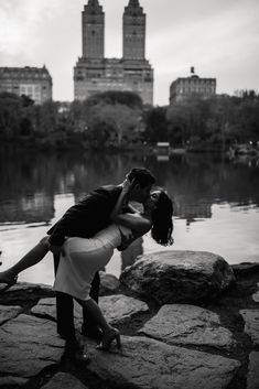 a man and woman kissing in front of a body of water with buildings in the background