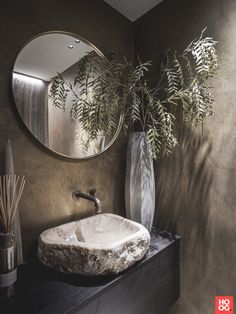 a bathroom sink sitting under a round mirror next to a vase filled with plants and reeds