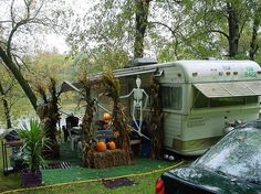 an rv is parked in the grass next to a tree stump with skeletons on it