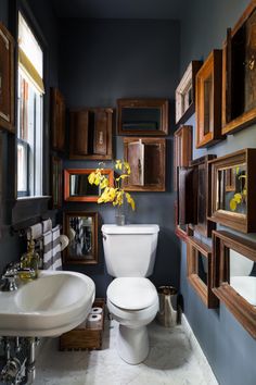 a white toilet sitting next to a sink in a bathroom under wooden framed pictures on the wall