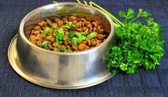 a metal bowl filled with dog food next to some parsley