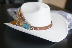 "Bridal Western Cowgirl Hat, ONE SIZE FITS ALL! It is a durable canvas material.  PLEASE NOTE THE BRIDAL VEIL IS NO LONGER AVAILABLE DUE TO LOW DEMAND. If you would like this feature added, please add \"bridal veil\" in the 'message seller' box before purchasing The leather strap has turquoise beads all around it, and on the right side there is a geode blue gem attached to the side, along with champagne (light and dark) colored beading, white beads (sparkly and plain white beading), gold colored tool with glitter embedded in the tool, and 3-4 feathers all attached by gorilla glue and hot glue. The hat also has a vinyl sticker attached to the right side of the hat to let everyone know you are the bride to be! There is an elastic strap on the inside of the hat to keep your head comfortable a Bridal Cowgirl, Bride Cowgirl Hat, Womens Western Hats, Western Bride, Ivory Bride, Bridal Hat, Felt Cowboy Hats, Gorilla Glue, Bohemian Bridal