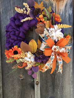 a purple wreath with orange and white flowers hanging on a wooden door handle that is attached to a fence