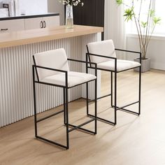 two white chairs sitting next to each other on top of a hard wood floor in front of a counter