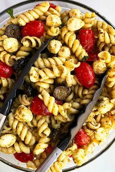 pasta salad with tomatoes and mushrooms in a glass bowl on top of a white table