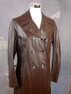 This long double-breasted brown soft leather trench coat has wide pointed notch lapels and closes in the front with three brown buttons (six in total show on the front).  The coat has a fitted waistline, and the back has a contouring faux half-belt and a 21-inch (53.34cm) inverted pleat to the hemline. The high-quality coat features topstitching and figure-enhancing contouring seams on the front and the back and is lined in a brown satin viscose fabric. Condition: Excellent (Professionally Cleaned ... soft and supple, with no stains, tears, wear spots, or weaknesses in the seams)   Size 8/10 US, 12/14 UK Bust = 39 inches (99.06cm)  Shoulders =  16 inches (40.64cm) Waist = 35 inches (88.9cm) Hips = 41 inches (104.14cm) Sleeve length = 24 inches (60.96cm) Coat length = 44 inches (111.76cm) B Brown Leather Trench Coat, Long Leather Jacket, Leather Trench, Brown Satin, Leather Trench Coat, Viscose Fabric, Soft Leather, Double Breasted, Dark Brown