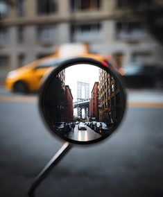 a rear view mirror on the side of a street with buildings and a yellow taxi