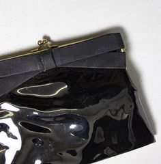 "Vintage chic and simple 1950s cocktail clutch purse. Black vinyl looks like patent leather with a ribbon bow. Angled shape. Gold colored metal frame with kiss lock closure. Lined in super cute black and white printed vinyl. Marked: none Length: 8\" Height: 6\" Depth: 1/2\" Condition: Very good. Some overall wear, wear to the edges and faint surface scratches. Please do not hesitate to convo with any questions. We upload large pictures - Simply click on each picture for a closer look. More VINTA Retro Black Evening Bag, Vintage Black Clutch For Evening, Vintage Black Evening Clutch, Retro Black Evening Bag For Formal Occasions, Retro Clutch Evening Bag For Events, Classic Black Clutch For Party, Black Vinyl, Clutch Purse, Cute Black