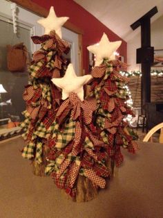 two christmas trees with white stars and plaid bows on them sitting in front of a fireplace