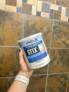 a person holding up a can of paint in front of a tiled shower stall wall