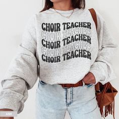 a woman wearing a sweatshirt that says choir teacher and has her hands in her pockets