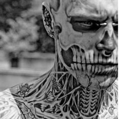 a black and white photo of a man with tattoos on his face, neck and chest