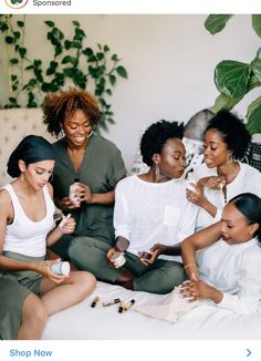 four women are sitting on a bed and one is looking at something in her hand