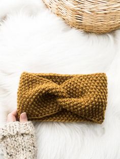 a hand holding a knitted headband on top of a white fur covered floor