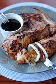 grilled chicken with onions and rice on a plate next to a cup of dipping sauce