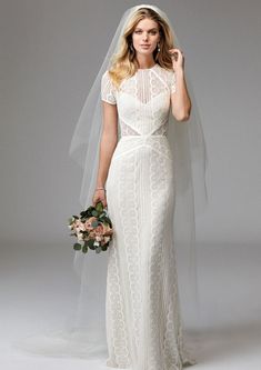 a woman in a white wedding dress holding a bouquet and looking at the camera while wearing a veil