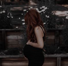 a woman with long red hair is standing in front of some flowers and looking at the ground