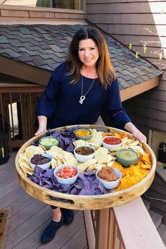 a woman holding a tray full of food on top of a wooden deck next to a building