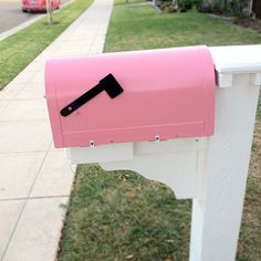 a pink and white mailbox sitting on the side of a road next to a sidewalk