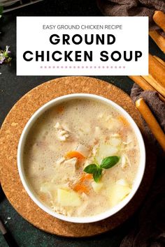 a close up of a bowl of chicken soup on a plate with carrots and bread sticks