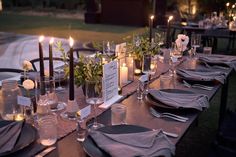 a long table set with place settings and candles for an outdoor dinner party in the evening