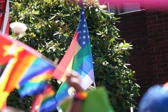 a group of people holding flags in front of a brick building with trees and bushes behind them