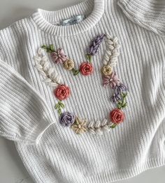 a white sweater with flowers on the front and back, sitting on top of a table