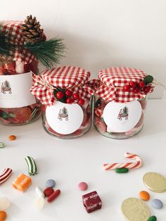 three jars filled with candy and candies on top of a white table next to christmas decorations