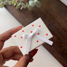 a hand holding a small white card with red hearts on it and a ribbon around the edge