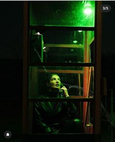 a woman sitting in front of a window talking on a cell phone