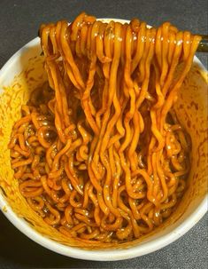 some noodles in a white bowl with sauce on top and chopsticks sticking out