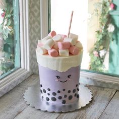 a cup filled with marshmallows on top of a table next to a window