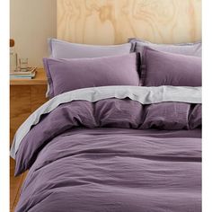 a bed with purple sheets and pillows on top of it in a bedroom next to a wooden headboard