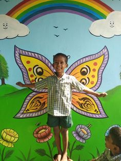 a young boy standing in front of a colorful wall with flowers and butterflies painted on it