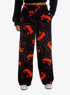 a person wearing black and orange pants with red dragon print on them, standing in front of a white background