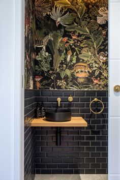 the bathroom is decorated in black and white with tropical wallpaper on the walls, along with a gold faucet