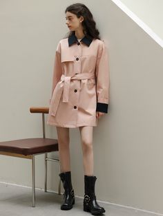 a woman standing next to a chair wearing a pink trench coat