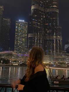 a woman is looking at the city lights and skyscrapers from across the river in front of her