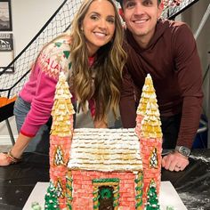 a man and woman posing in front of a gingerbread house