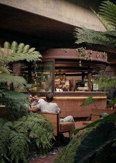 a man sitting on a bench in front of a bar surrounded by plants and trees