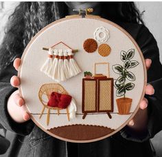 a woman is holding up a embroidery hoop with various items on it and a plant